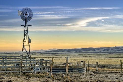 windmill with a pump and cattle water tank, dusk over prairie and foothills of northern Colorado