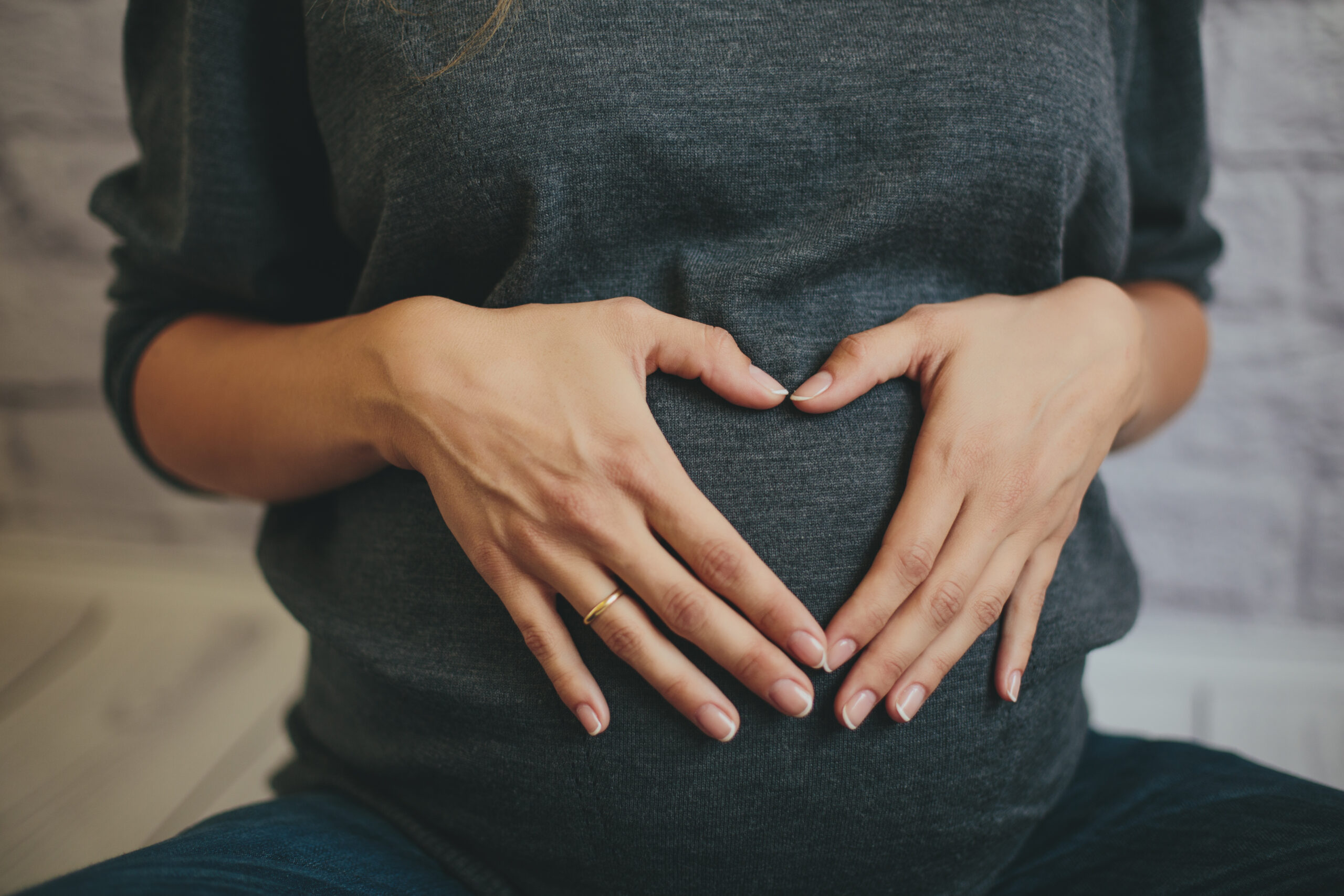 Pregnant person making a heart on stomach with hands